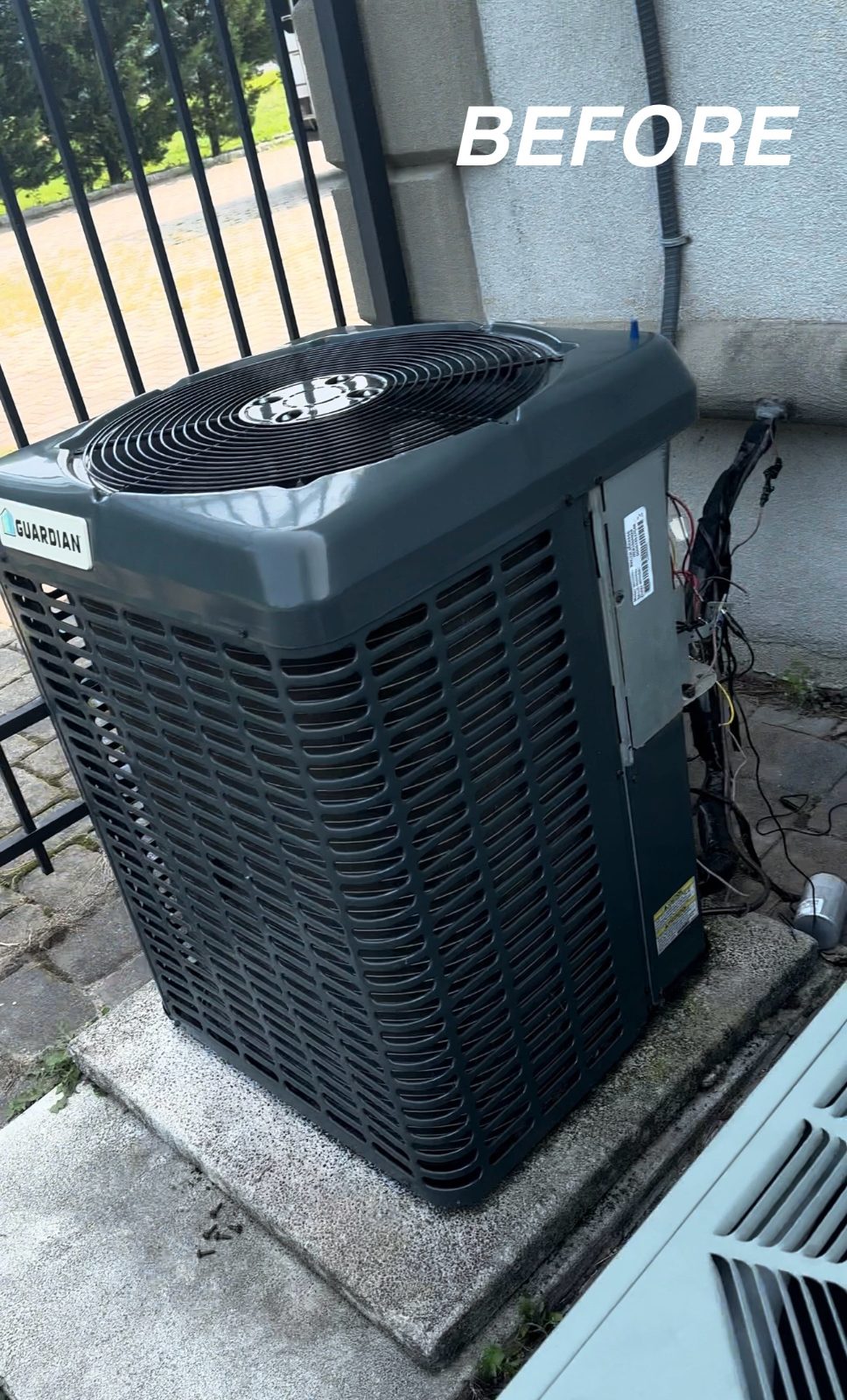 Old outdoor condenser behind a side gate before replacement