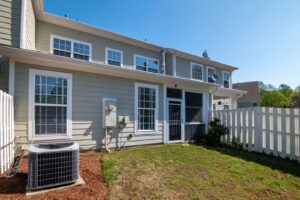 Outdoor air conditioning condenser unit on the lawn beside a suburban home with white fencing